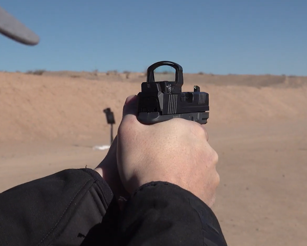 Close-up view of a shooter aiming the Ruger RXM with a mounted red dot sight at an outdoor shooting range.