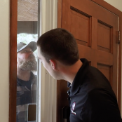 Man cautiously checking a bearded stranger outside his front door through a side window, highlighting a potential home defense scenario.