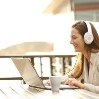 Side view portrait of a happy woman on vacation learning or having a video call with a laptop and headphones